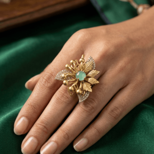 Elevate your jewelry collection with our Stunning Floral Leaf Statement Ring, a handcrafted masterpiece designed to bring luxury and charm to any festive or special occasion. Crafted with intricate gold-plated textured leaves and adorned with sparkling pavé CZ accents, this botanical statement piece features a gorgeous center stone available in two vibrant colors. Designed for versatile comfort, this adjustable ring pairs effortlessly with traditional ethnic wear, contemporary fusion outfits, and bridal ensembles. Explore our complete Artificial Jewelry Collection to find matching earrings and accessories, or learn more about classic Indian Kundan & CZ jewelry craftsmanship. Key Features: Design: Intricate textured leaf pattern with pave-set CZ stones and center gem. Finish: Premium high-polish gold plating for long-lasting brilliance. Fit: Comfortably adjustable band to fit most finger sizes. Style: Perfect for weddings, receptions, parties, and festive celebrations.